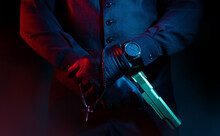 Photo Of A Male Mafia Criminal Killer In Suit And Leather Gloves Holding A Gun With Cross On Black Background.