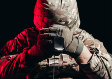Photo Of A Military Soldier In Uniform And Armor Helmet Sitting And Holding Metal Army Necklace On Back Background With Red Glow.