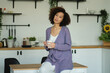 © yavdat - Happy woman holding a cup of coffee in her kitchen. Young african american female drinking coffee
