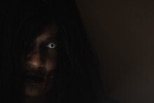 Female Zombie In Blood. Closeup Face And Eyes Of Asian Woman Ghost With Blood. Horror Creepy Scary Fear In A Dark House. Hair Covering The Face, Halloween Festival Concept