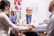 © DC Studio - Senior doctor giving bad news to young couple during medical check in hospital office. Husband and wife holding hands. Nurse looking at patient x-ray.