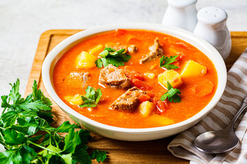 Wall Mural - Soup with beef and vegetables in white plate on a wooden board. Traditional meat shurpa soup with vegetables and herbs.