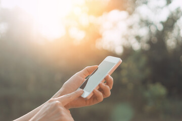 Wall Mural - Woman hand using smart phone at outdoor nature park with sunset sky abstract background.