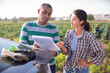 © JackF - Female farmer discussing some papers with hispanic partner while standing near car on farm field
