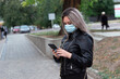 © Nikolay - girl in a medical mask on a city street looks at the phone