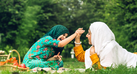 Wall Mural - Portrait of happy religious enjoy happy love asian family arabic muslim mother and little muslim girls child with hijab dress smiling and having fun moments good time in summer park