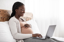Charming Pregnant Woman Relaxing With Her Laptop, Browsing Or Chatting With Friends Online, Sitting On Bed, Panorama With Empty Space