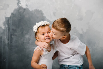 Happy children in denim casual style clothes. Boy wearing jeans isolated on grey wall indoors. Kids hugging. Brother kiss sister.