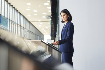 Side view portrait of contemporary Middle-Eastern businesswoman swiping phone while passing turnstile gate in airport or office building, copy space