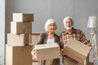 © LIGHTFIELD STUDIOS - senior couple holding cardboard boxes and looking at camera in new house, moving concept
