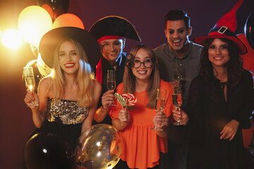 Wall Mural - Happy friends in costumes enjoying Halloween party on dark background