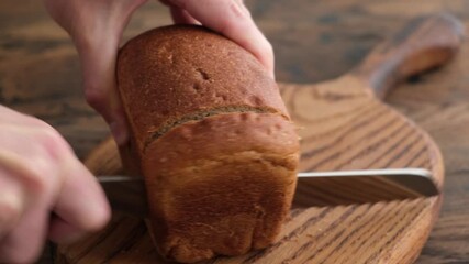 Canvas Print - Cutting loaf of sourdough bread with sharp bread knife on a wooden table background