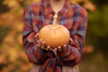 A Girl Holds A Small Pumpkin In Her Hands. Shallow Depth Of Field.
