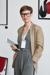 Wall Mural - Vertical portrait of elegant creative woman smiling at camera and holding digital tablet while planning art gallery exhibition, copy space