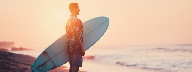 Wall Mural - Man surfer on the beach near the ocean watching sunset. Wide screen, panoramic