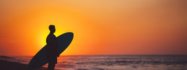 Wall Mural - Silhouette of man surfer on the beach near the ocean watching sunset. Wide screen, panoramic