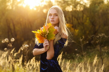 beautiful female holding autumn maple leaves in forest. young blonde woman with European appearance and perfect facial features on a background of autumn nature. close-up portrait. 