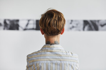 Wall Mural - Graphic back view portrait of tattooed young woman looking at paintings at contemporary art exhibition, copy space