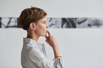 Graphic side view portrait of tattooed young woman looking at paintings at contemporary art exhibition, copy space