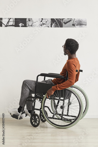 Minimal full length portrait of young African-American man using wheelchair and looking at paintings while exploring modern art gallery exhibition