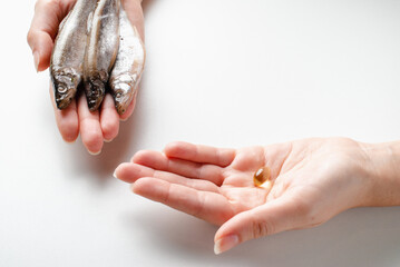 Wall Mural - Young woman is holding fish and omega 3 pills in hands. Healthy food, Choose between food or capsule.
Place for the text.