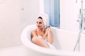 Wall Mural - Beautiful young woman in bathrobe lying in bathtub. Self care concept.