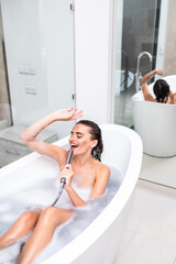 Wall Mural - Young woman in foam bath having fun singing white lying in bathtub