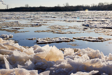 Ice drift on a river with blue high water and big water, white snow broken ice full of hummocks in it and sun reflection in sunny spring day.