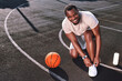© Afshar Tetyana - Joyful man tying his shoelaces on a basketball court