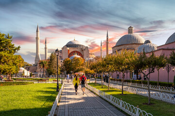 Tourists walk through the Hippodrome towards the ancient mosque, church and museum of Hagia Sophia in Sultanahmet Square at sunset, Istanbul Turkey