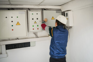 Wall Mural - An electrician in an engineering helmet opens the switch box. The technician works in the electrical control room. Service of power distribution switchboards. Back view