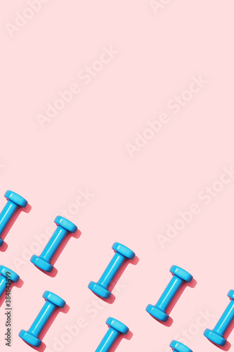 Pattern blue dumbbells on a pink background top view. Fitness gymnastic equipment for female home workouts and exercises. An accessory for home sports and a healthy lifestyle. Copy space