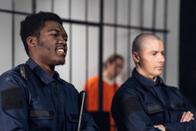 Prison Guards Smile As They Stand With Batons Near Cells With Dangerous Criminals. Multi-racial Portrait