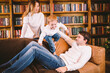 © Elizaveta - Christmas family portrait. Young Caucasian family in identical clothes having fun on sofa in living room with large library of books and Christmas tree in evening. Happy New Year and Merry Christmas