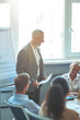 © Kostiantyn - Vertical shot of a confident mature businessman holding document and smiling while discussing new project with collegaues