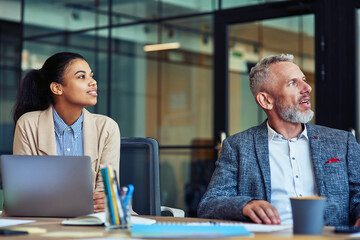 Fototapete - Business people at work. Young mixed race woman and her mature colleague looking away while sitting at desk and working together in the mode office