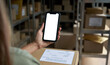 © insta_photos - Female warehouse worker seller, small stock business owner holding phone mock up screen ad scan retail package parcel bar code on commercial shipping box delivery order on smartphone using mobile app.