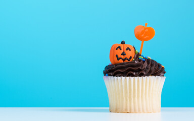 Wall Mural - Cupcake on Halloween party. Dessert decorated with chocolate cream, candy shaped pumpkin Jack-o-lantern frosting or Icing. Cupcakes on blue background. Happy Halloween!!!