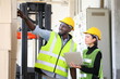 © Akarawut - African American and Asian workers wearing safety vest while working in warehouse checking for the inventory of product using laptop for industrial business