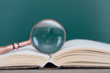 There is a magnifying glass on the book opened in front of the blackboard