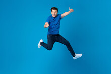 Smiling Handsome American Man Joyfully Jumping And Doing Double Thumbs Up Gesture Isolated On Blue Studio Background