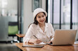 © amnaj - Portrait of pretty young asian woman wearing a white hat taking note and using laptop computer at home. Female student studying online at home.