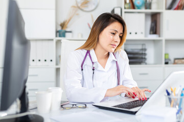 Wall Mural - Woman doctor in uniform is working behind laptop in clinic