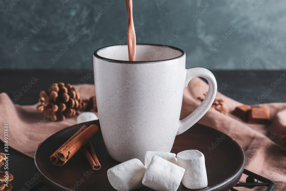 Pouring of hot cocoa drink in cup on table