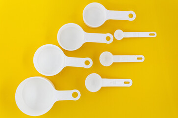 Set of white measuring cups, measuring spoons use in cooking lay on wooden yellow background in top view