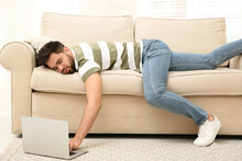 Lazy Young Man Using Laptop While Lying On Sofa At Home