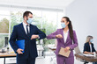 © New Africa - Office employees in masks greeting each other by bumping elbows at workplace