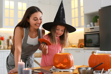 Canvas Print - Mother and daughter making pumpkin jack o'lantern at table in kitchen. Halloween celebration