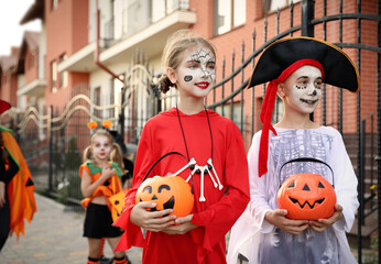 Poster - Cute little kids with pumpkin candy buckets wearing Halloween costumes going trick-or-treating outdoors