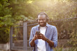 © YURII MASLAK - Walking in the street, relaxation, leisure. Young Afro-American man in headphones listening music on smart phone using music app. Portrait of smiling guy in earphones and mobile phone outdoors.